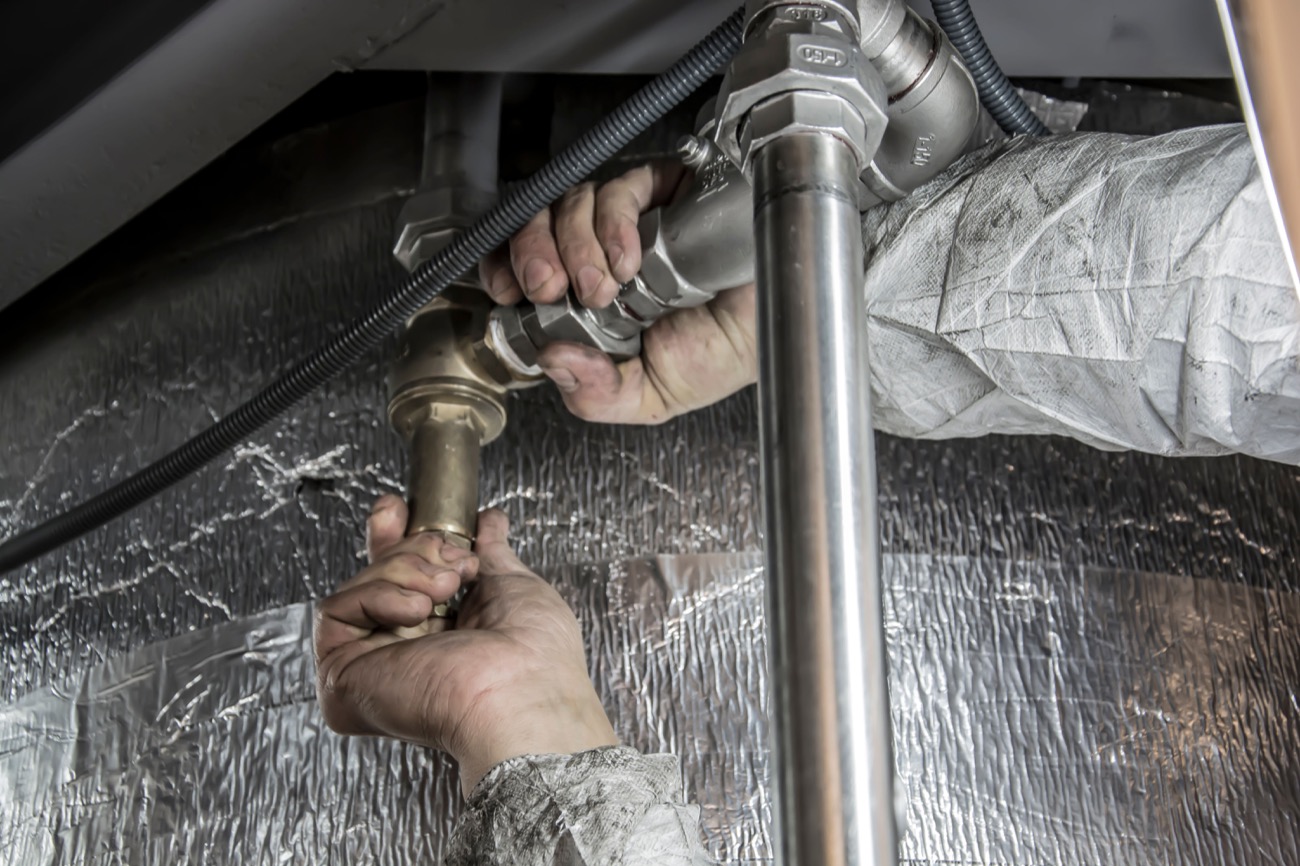 Hands repairing metal plumbing pipes under a home