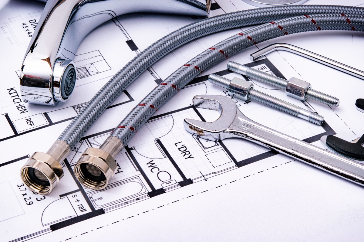 Plumbing fixture, braided supply lines, and wrench resting on home plans